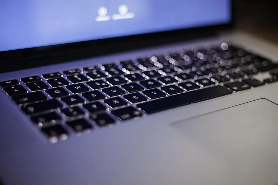 Close-up of a laptop keyboard with backlit keys, the screen glowing blue above it