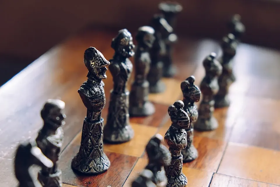 Carved metal chess pieces lined up on a wooden chessboard, in shallow focus