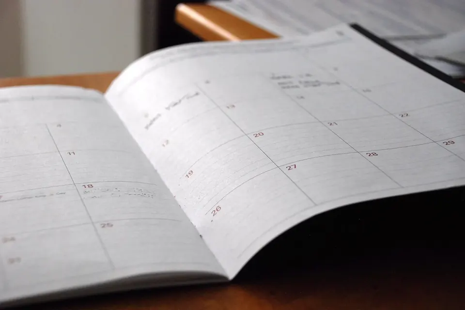 An open monthly planner on a wooden desk, its blank date grid in soft focus