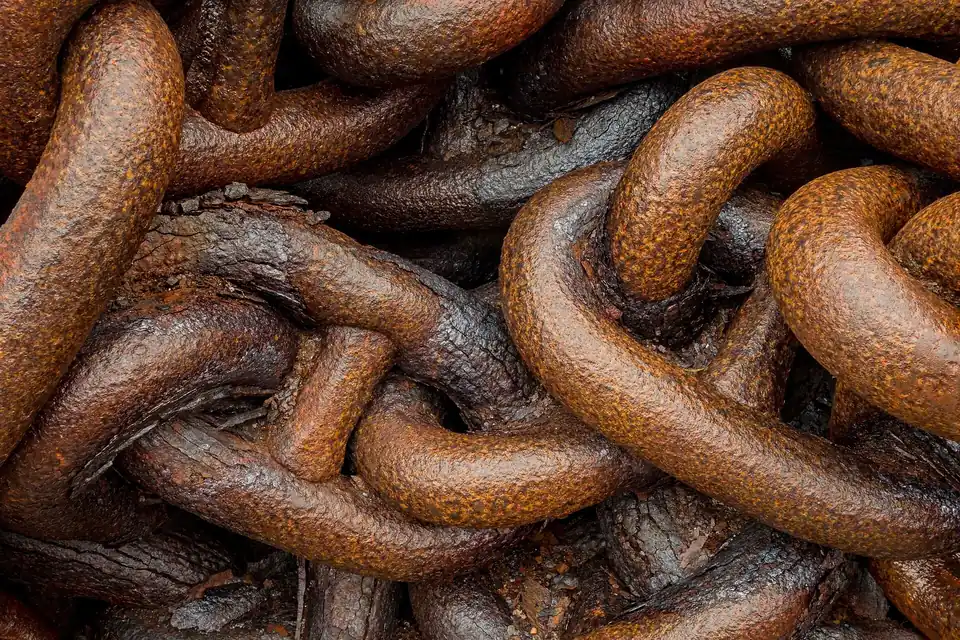 Close-up of heavy, deeply rusted chain links piled on top of each other, wet from the rain
