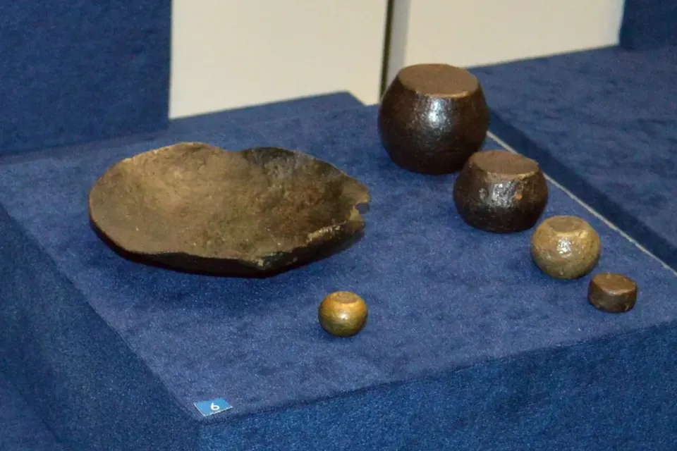 A bronze weighing pan and a set of round weights of decreasing size displayed on a blue cloth