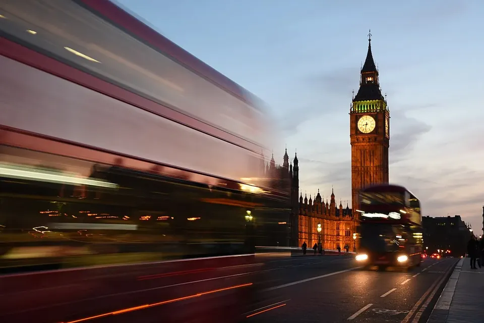 The Elizabeth Tower and the Houses of Parliament at dusk, with a red double-decker bus passing in a motion blur